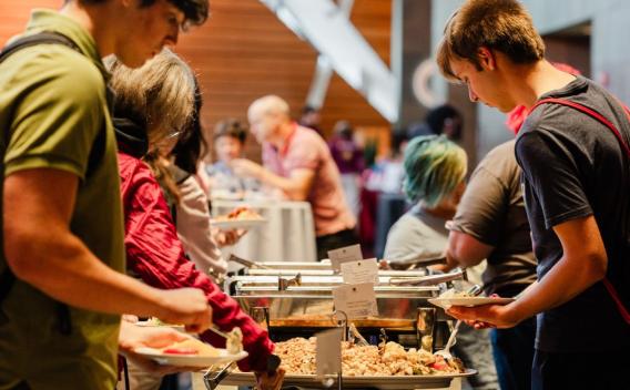 Students fill their plates at a buffet table during a university event.