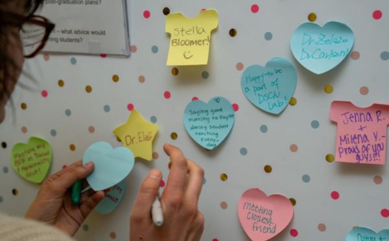 A student writes a message of hope on a community banner filled with positive messages on heart shaped post-it notes.