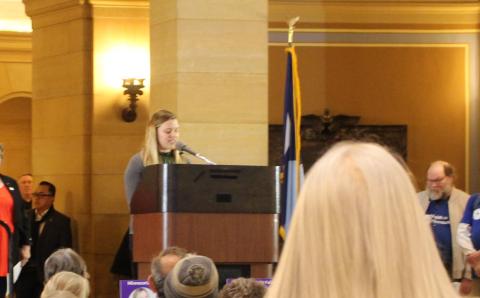 Assistant Professor Hannah MacDougall speaks at the Minnesota state capitol to an audience of residents lobbying for medical debt relief.