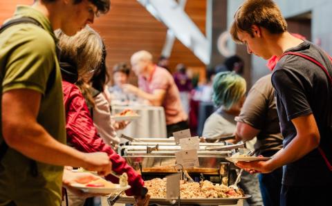 Students fill their plates at a buffet table during a university event.
