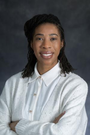 Channel Lowry, PhD candidate, wears a which shirt and a white sweater and smile in this professional portrait.