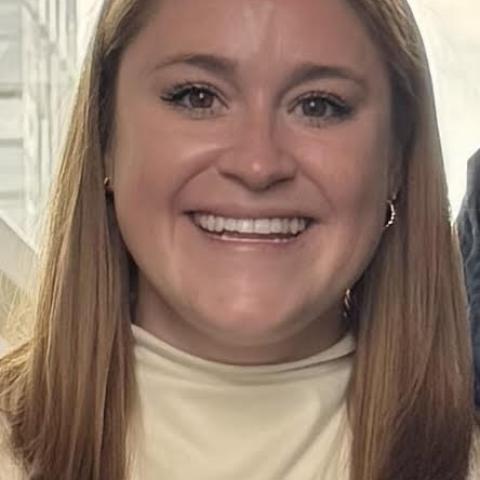 Melissa Latcham, PhD candidate, smiles and wears a cream colored shirt in this professional portrait taken in a downtown office building.