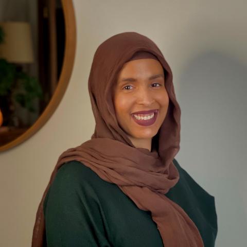 Johara Suileman, PhD candidate, wears a brown hijab and a green dress and smiles in this professional portrait.